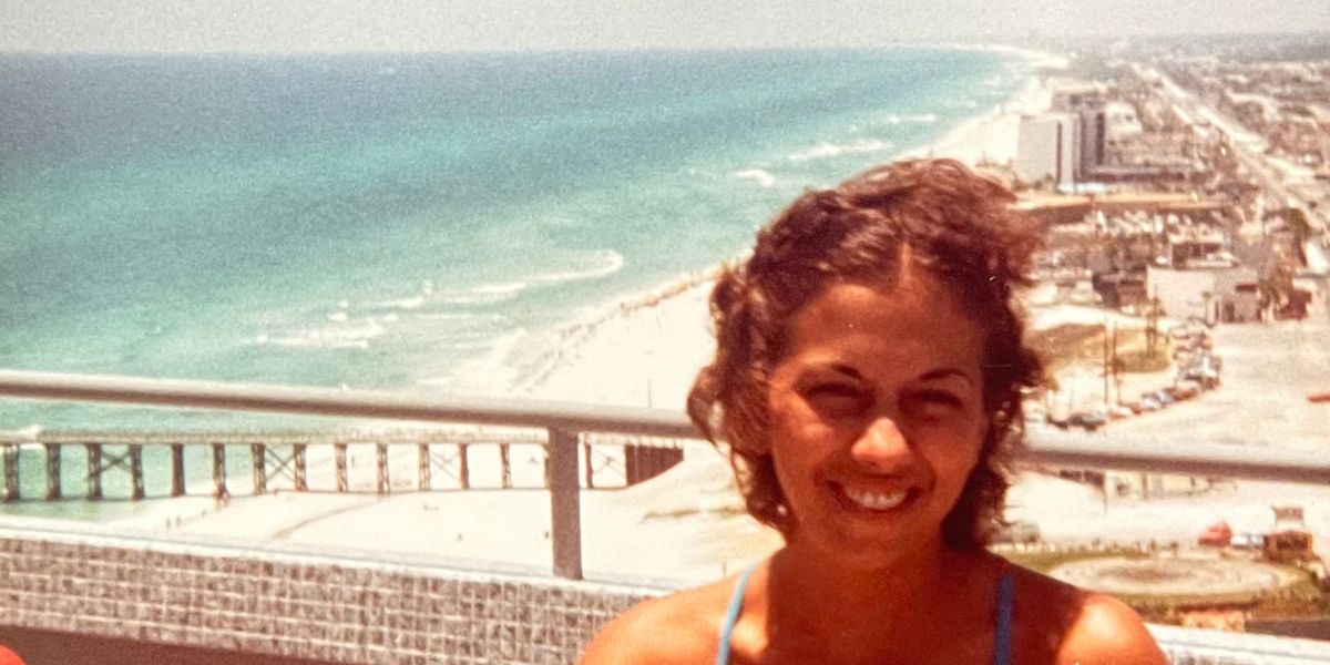 In a sunny photo from 1976, a young woman stands on a balcony overlooking the shoreline and city behind her.