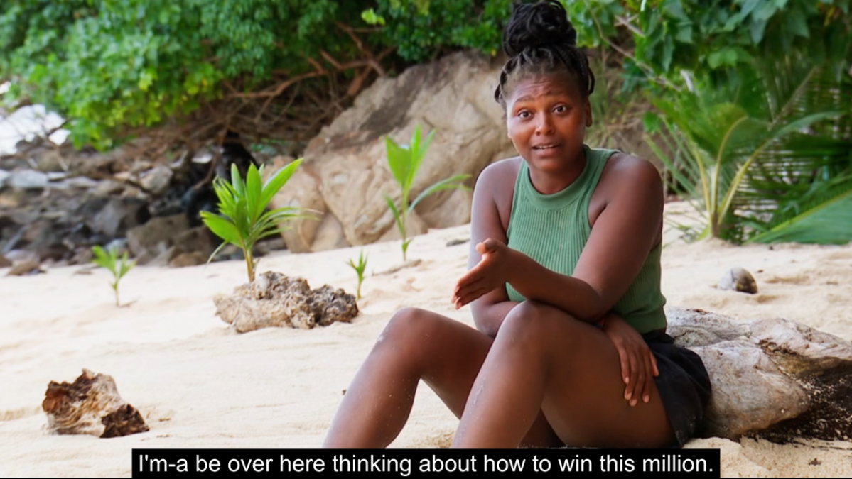 Survivor Season 45 contestant Katurah Topps sits on the beach, addressing the camera, explaining that while Dee and Austin are canoodling, she’ll be “over here thinking about how to win this million.”