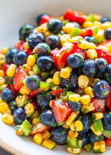 A colorful bowl of fruit and corn salad with strawberries, blueberries, corn kernels, and chopped green peppers.