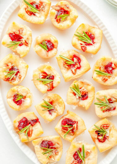 Cranberry Brie Bites - The perfect two-bite holiday appetizer recipe with melted brie cheese, sweet-tart cranberry sauce, and fresh rosemary all nestled inside a buttery soft crust! An EASY appetizer recipe with just 4 main ingredients that's ready in 30 minutes! PERFECT for Thanksgiving celebrations, holiday and Christmas parties, or for New Year's Eve!