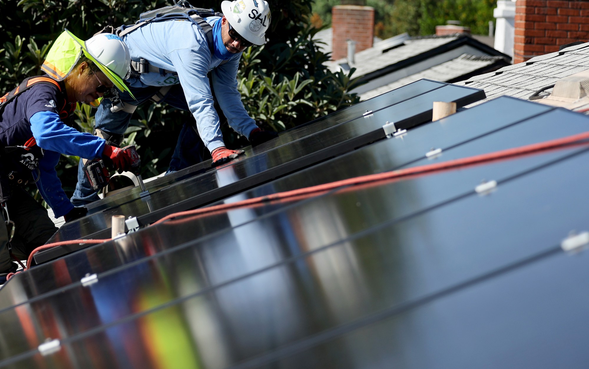 POMONA, CALIFORNIA - OCTOBER 19: GRID Alternatives employees Tony Chang (L) and Sal Miranda install no-cost solar panels on the rooftop of a low-income household on October 19, 2023 in Pomona, California. GRID Alternatives has installed no-cost solar for over 29,000 low-income households located in underserved communities which are most impacted by pollution, underemployment and climate change. They are the country's biggest nonprofit clean energy technologies installer and operate in California, mid-Atlantic states and Colorado. (Photo by Mario Tama/Getty Images)