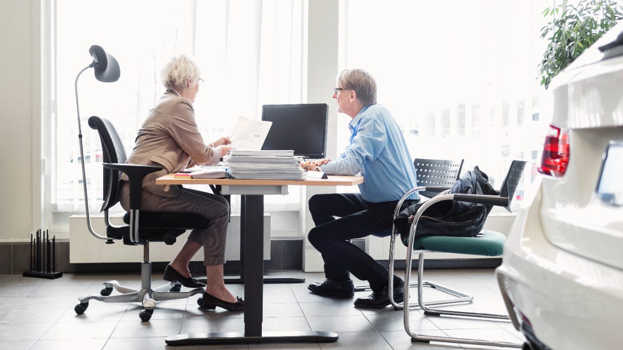 Woman and man sitting at table in car dealership, woman explaining documents