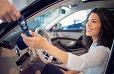 Smiling woman sitting in driver's seat accepting a key from hand off camera