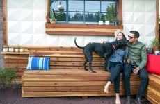 Happy couple holding beer bottles playing with dog while sitting in backyard of home