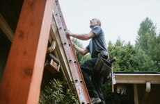 A man on a ladder climbing up to the roof.