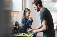 Side view of father cooking food while daughter having apple in kitchen