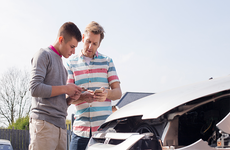 Two people looking at phone in front of damaged car