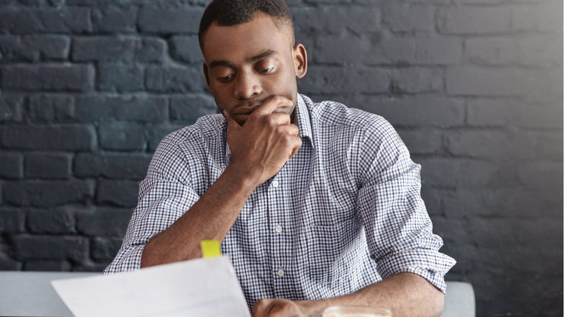 Young man with ponderous expression reviewing paperwork