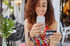 Smiling young woman holding phone and credit card