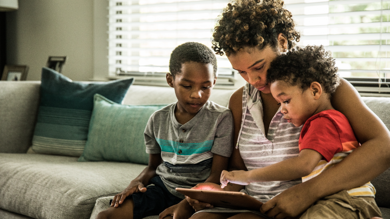 Mother using tablet with young sons on couch