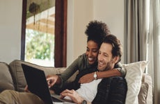 A happy young couple using a laptop while relaxing on a couch in their living room at home