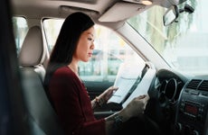 Driver sitting in their car with the window down, reviewing documents. The car is not in motion.