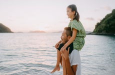 Father carrying young daughter on shoulders on beach at sunset