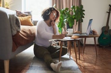 Young woman sitting in living room while working on laptop with headphones on