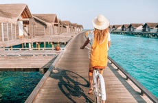 Young woman riding bicycle on wooden pier in the Maldives