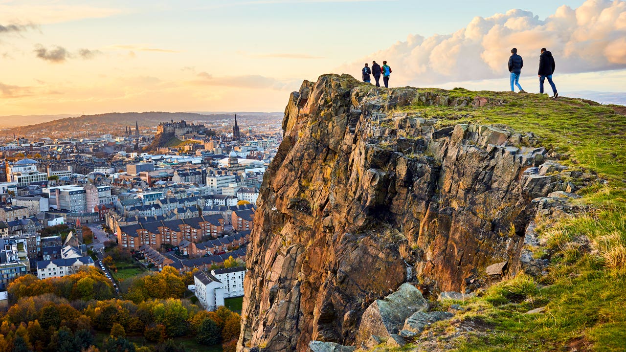 Group of people walking along cliff edge looking at Edinburgh city views