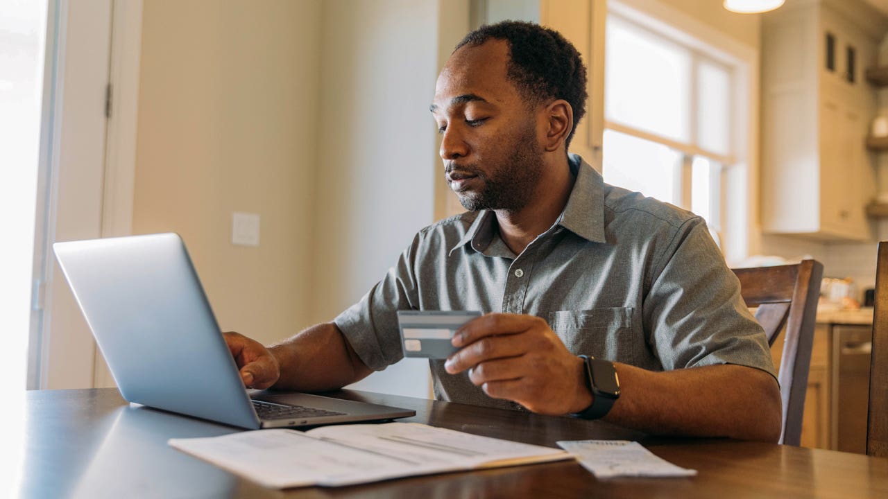 man working on laptop and holding credit card