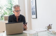 Man sitting in home office, using laptop and cell phone