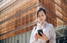 Well-dressed woman in front of big building smiling down at phone