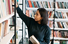 Young female african american librarian making order on bookshel