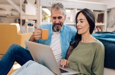 A man and a woman sit on a couch and look at a laptop together