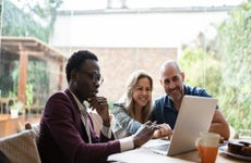 Real estate agent in businesswear working on a laptop with a couple in their home at the kitchen table