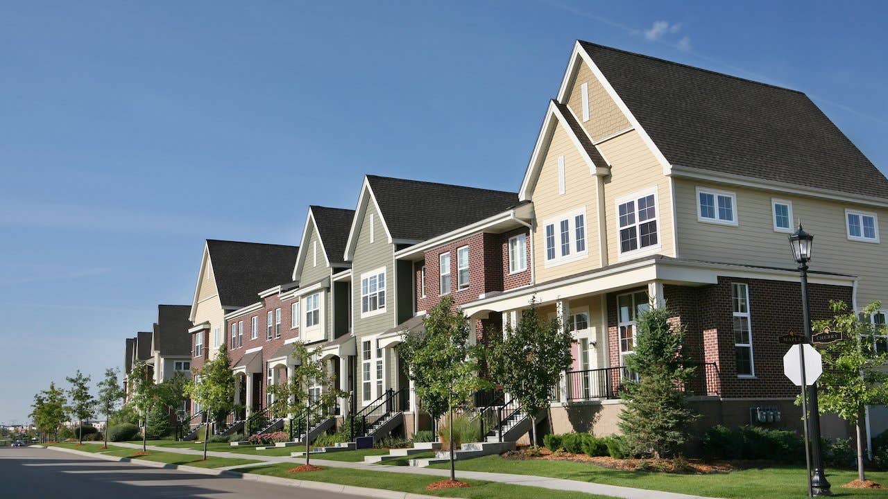 A row of tidy suburban townhouses, with newly planted trees and a blue sky