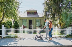 Young mother and father walking with baby daughter in stroller on neighborhood sidewalk