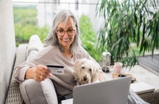 Senior woman with laptop and dog outdoors on balcony at home, making online payment.