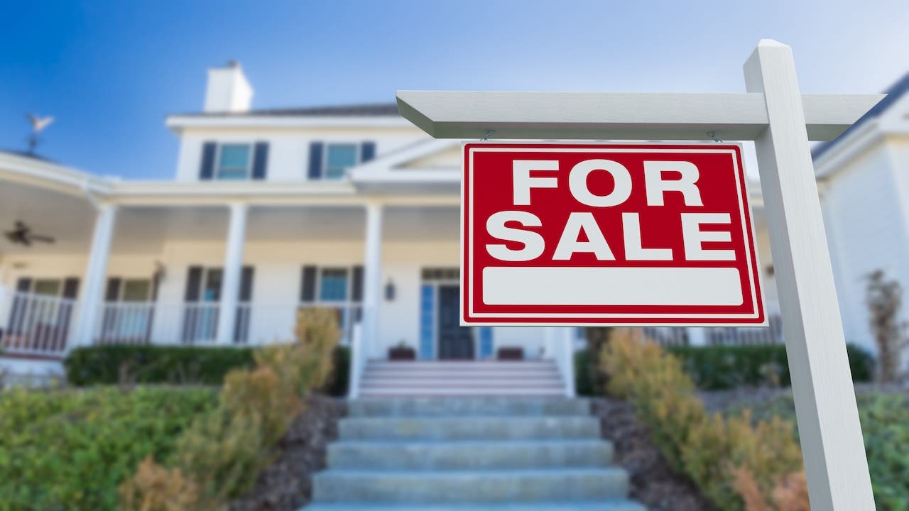 white suburban house with red for sale sign looking up front steps