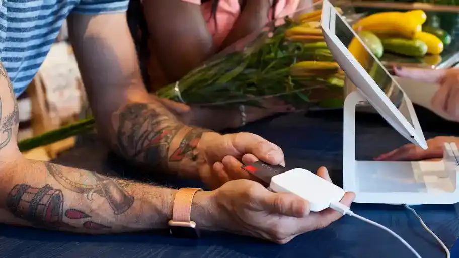 A man inserting his payment card into a card reader at a point-of-sale terminal. He is using the card reader to make a payment transaction.