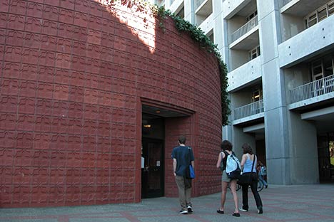 Circular reddish building with people walking toward the entrance