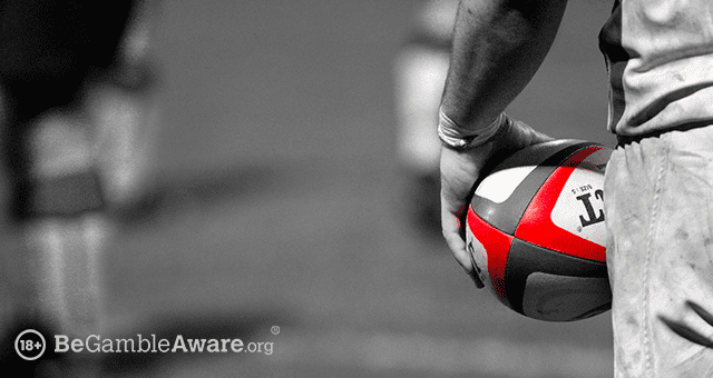 a closeup of a player's hand holding a rugby ball