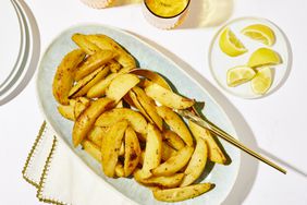 Greek Lemon Potatoes on blue dish next to plate of lemons