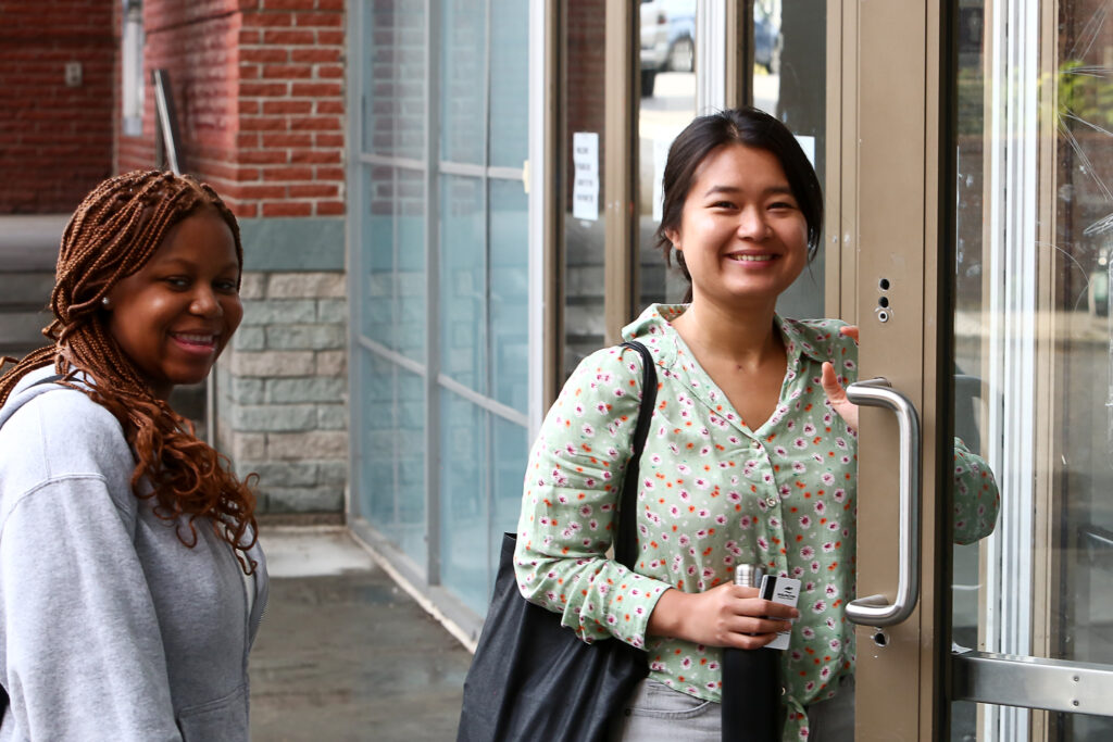 2 women smiling at the camera while opening a door