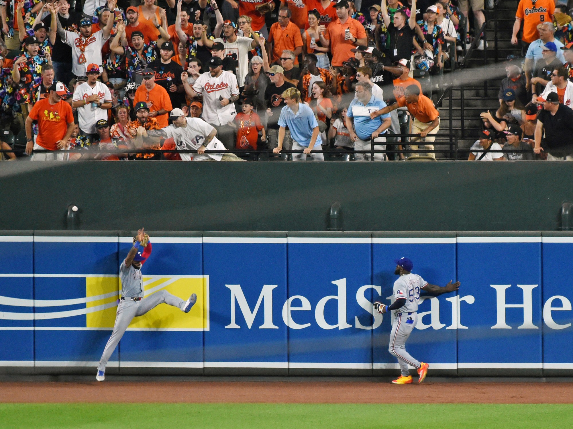 Orioles Heston Kjerstad's fifth inning grand slam is out of the reach of Texas Rangers center fielder Derek Hill. Right fielder Adolis Garcia watches fans reach for the ball at Orioles Park at Camden Yards. (Kim Hairston/Staff)