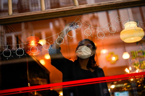 Graphic designer Chloe Vanhoecke, wearing a face mask to prevent the spread of the coronavirus COVID-19, works on Christmas decorations in a restaurant window in downtown Brussels, Wednesday, Dec. 2, 2020. In Belgium, experts say wearing masks and practicing social distancing will be essential in containing the spreading of the virus when shopping returns to a sense of normalcy. (AP Photo/Francisco Seco)