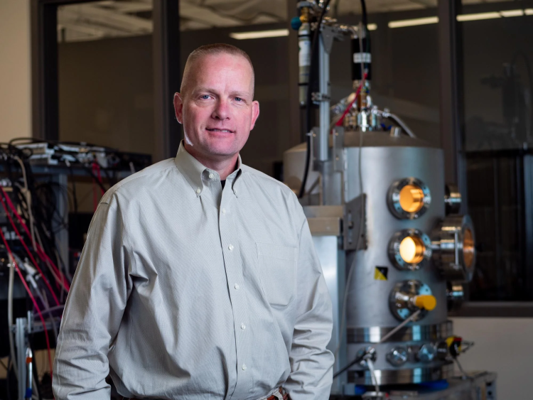 Hanspeter Schaub standing in a lab with large apparatus behind him