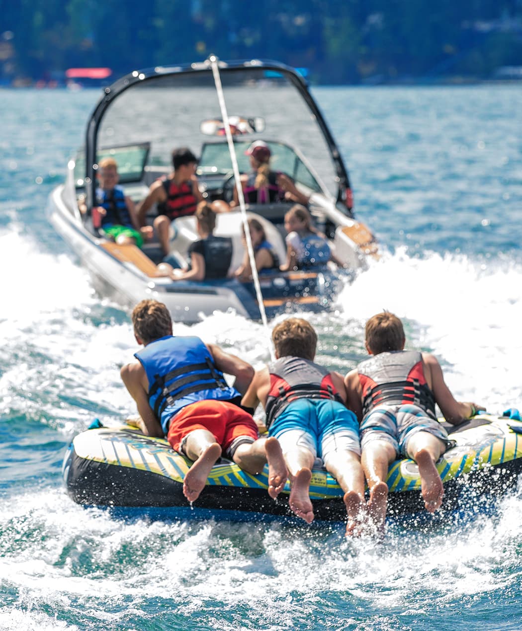 three boys enjoying riding a tube pulled by a boat on lakewater