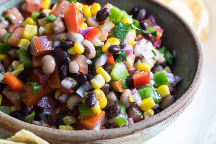 Cowboy caviar in a bowl on a white plate with tortilla chips.