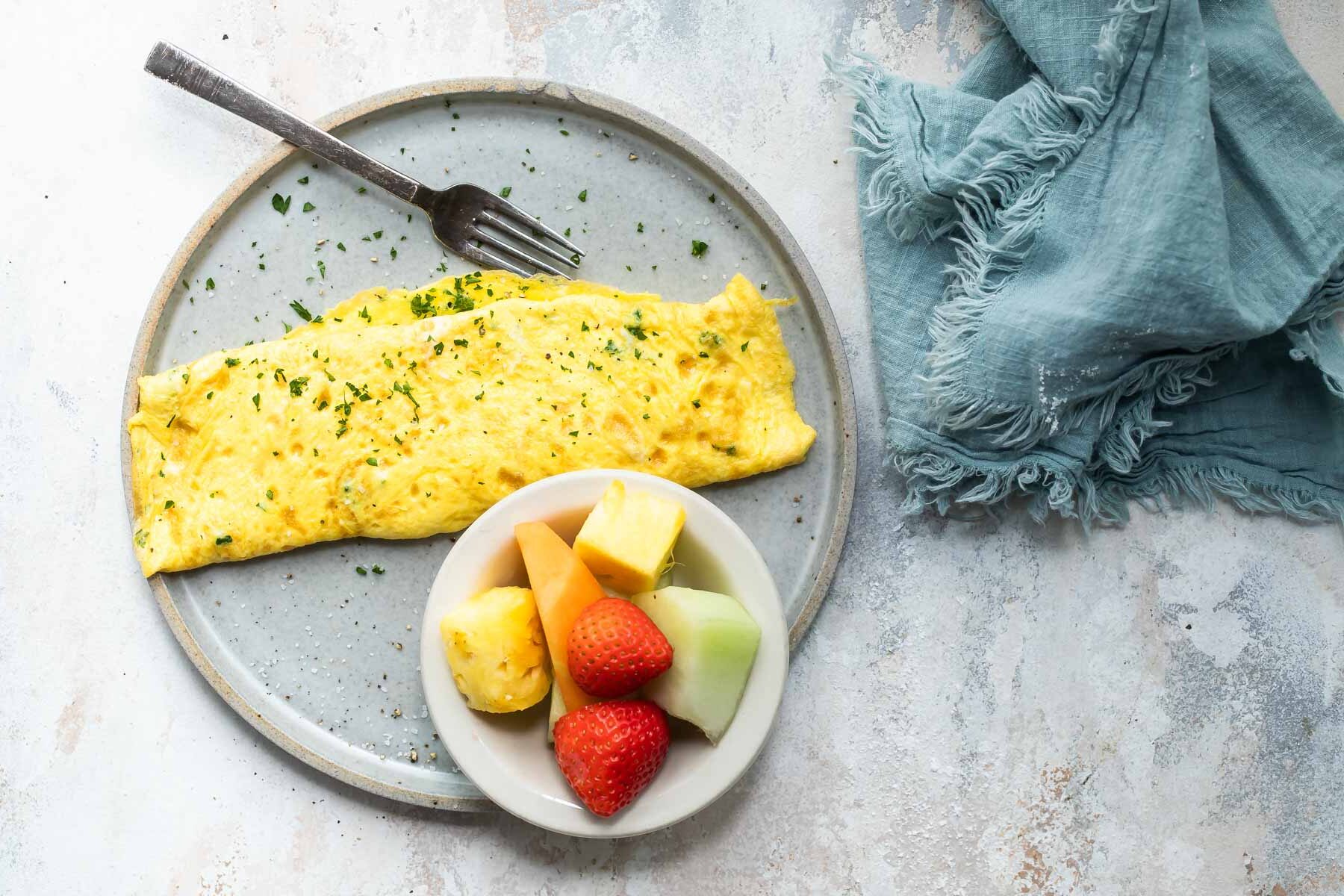 An omelet on a gray plate with a side of fruit.