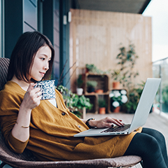 Femme sur un patio utilisant son ordinateur portable en dégustant un café