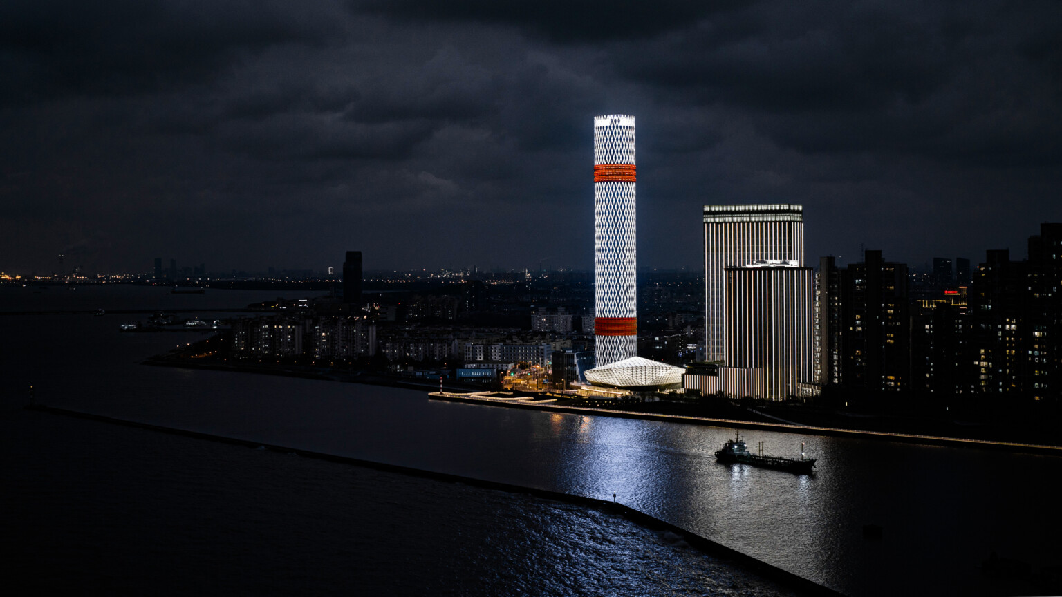 Boashan Long Beach Complex illuminated at night along Shanghai's Yangtze River, diamond geometric light on cylindrical tower