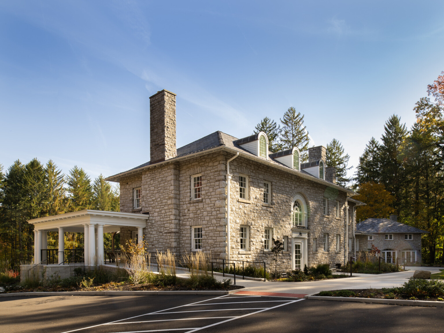 Stone façade mansion nestled in lush, tall trees, greenery, blue skies