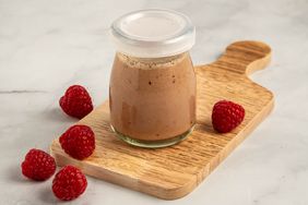 Angled view of a jar of Raspberry Vinegar Dressing recipe on a wooden cutting board with several raspberries