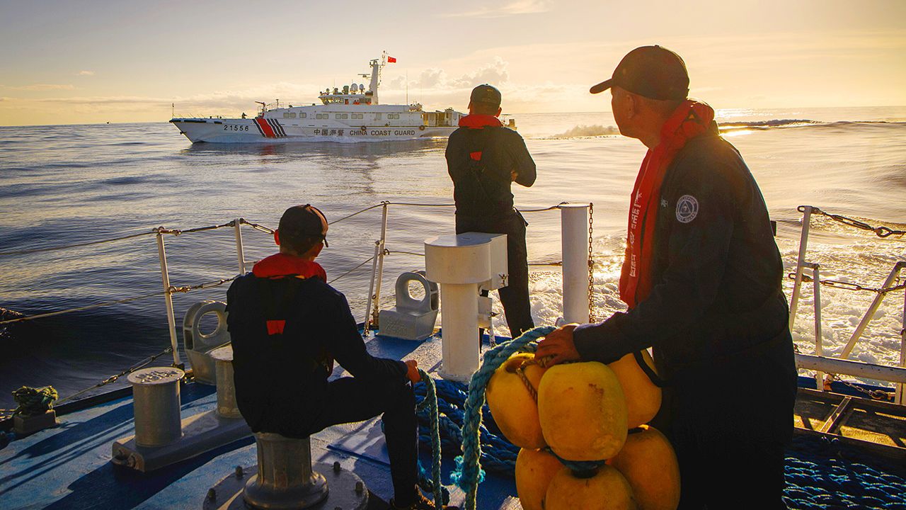 Crew aboard a Philippines Coast Guard vessel watch a Chinese Coast Guard ship in waters off the Philippines