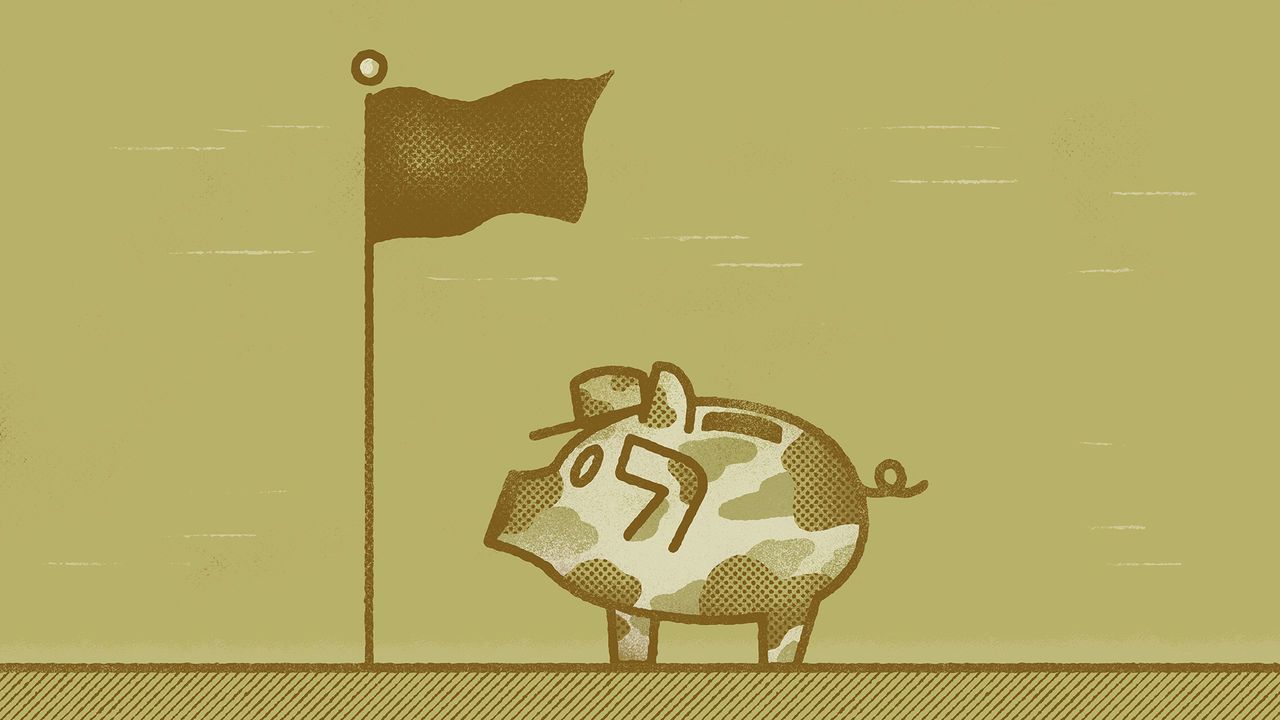 A camouflaged piggy bank wearing a baseball cap stands in front of a flag on a flagpole.