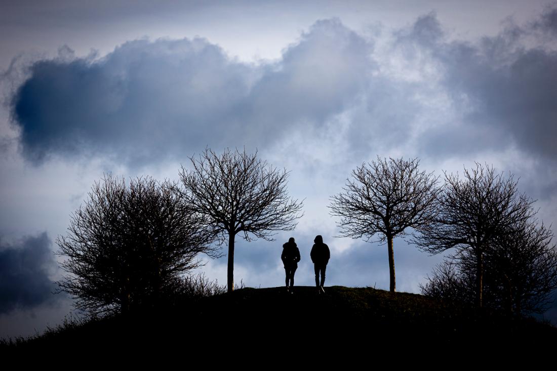 Spaziergänger gehen einen Hügel hinauf, während bei stürmischem Wetter dunkle Wolken am Horizont vorbeiziehen. (Symbolbild)