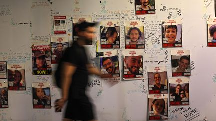 Un homme passe devant des portraits d'otages israéliens affichés sur un mur à Tel Aviv le 21 novembre 2023. (AHMAD GHARABLI / AFP)