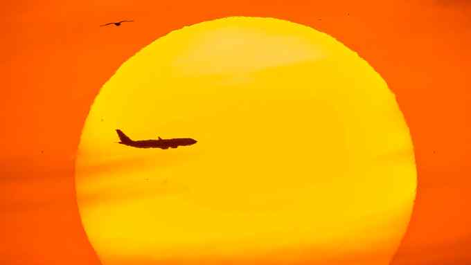 A passenger aircraft is silhouetted by the setting sun